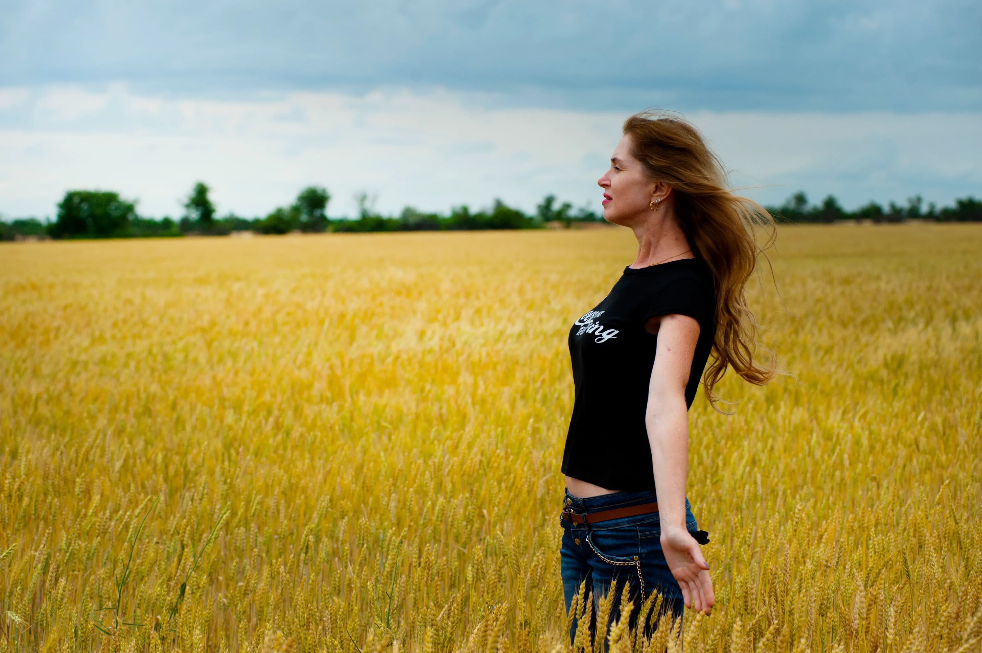 A woman standing in a field beneath a cloudy sky, looking toward the open horizon.