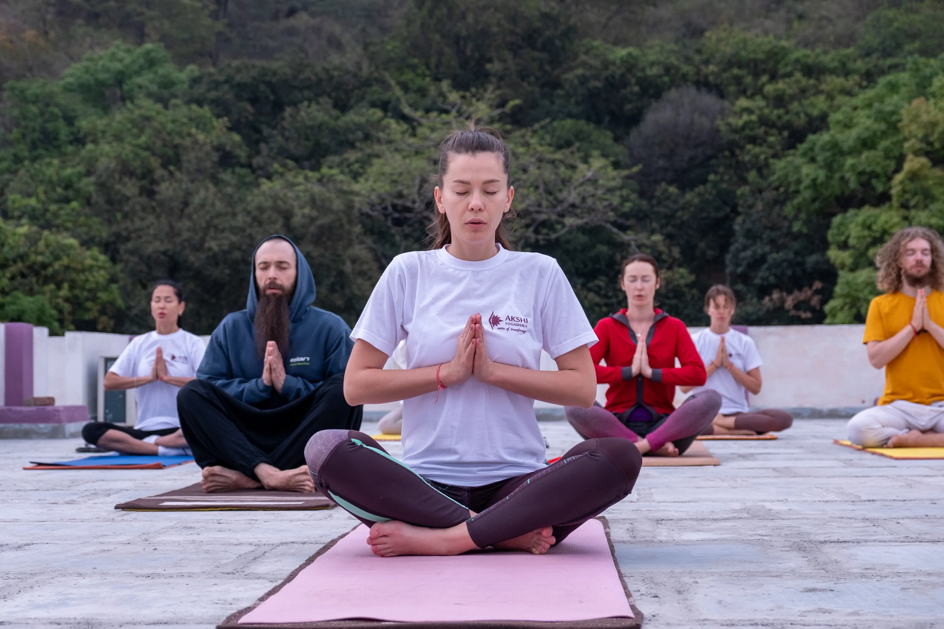 People practicing meditation together outdoors in a seated yoga pose.