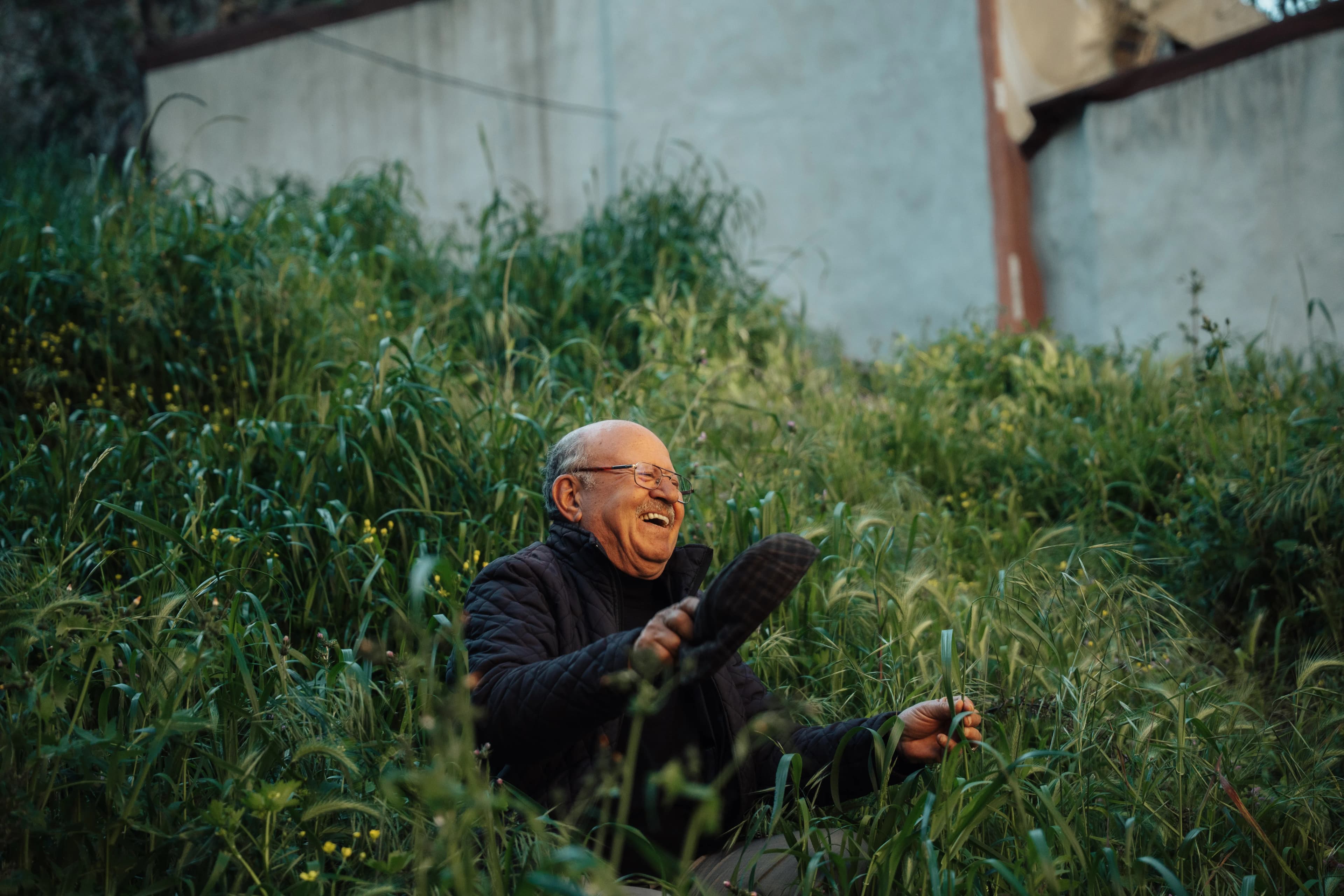 Older man laughing while sitting in overgrown grass, symbolizing letting go and finding freedom.